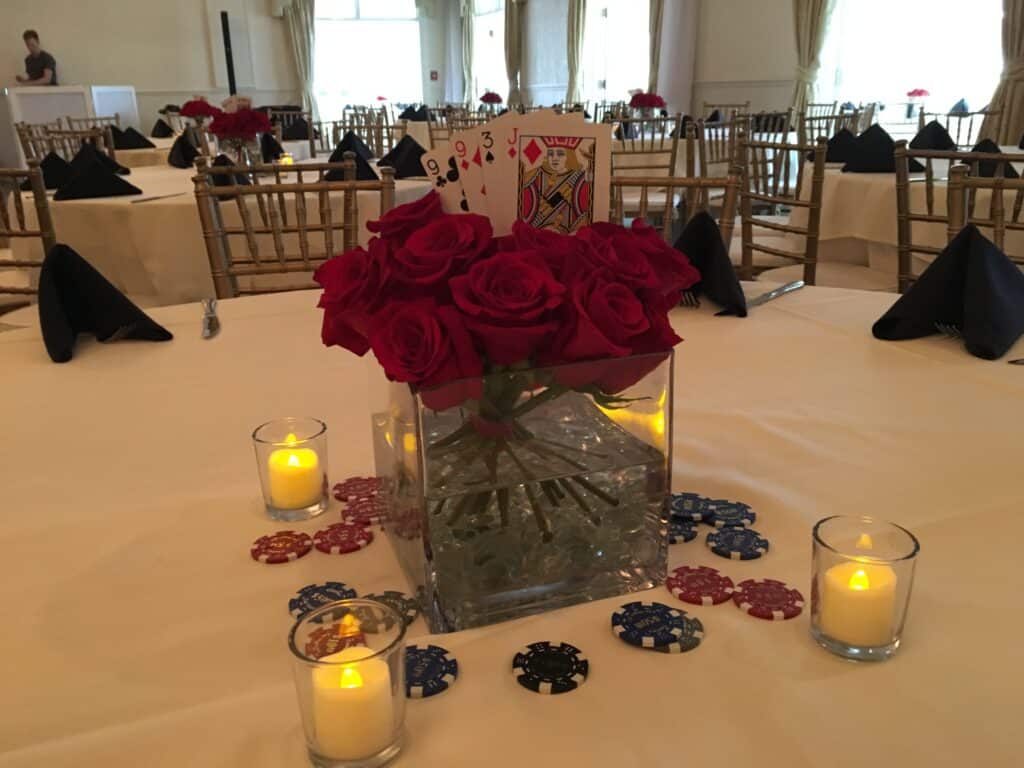 Glass cube filled with red roses and accented with four playing cards and loose chips